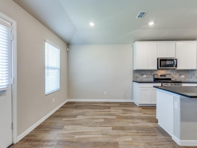 kitchen with vaulted ceiling, appliances with stainless steel finishes, white cabinets, backsplash, and light hardwood / wood-style floors