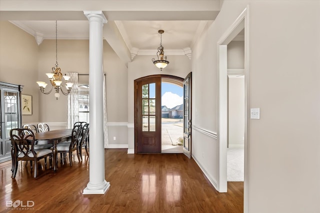 entryway with ornate columns, crown molding, dark wood-type flooring, and a notable chandelier