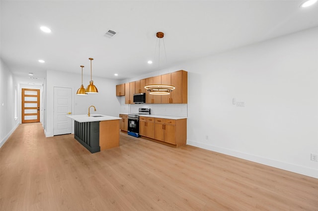 kitchen featuring sink, a center island with sink, pendant lighting, stainless steel appliances, and light hardwood / wood-style floors