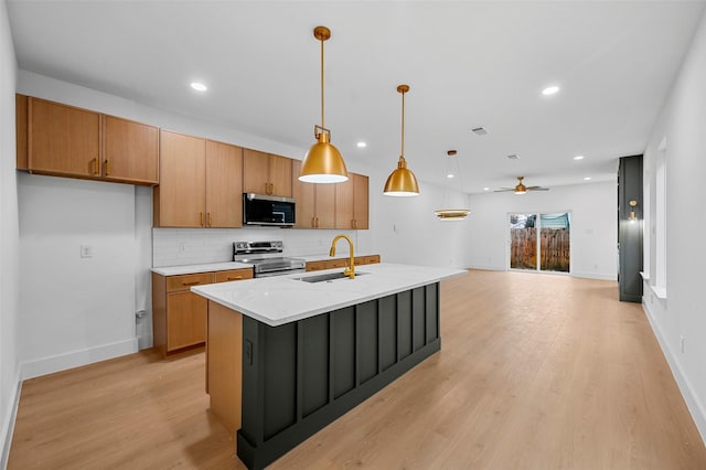 kitchen featuring pendant lighting, sink, appliances with stainless steel finishes, light stone counters, and an island with sink