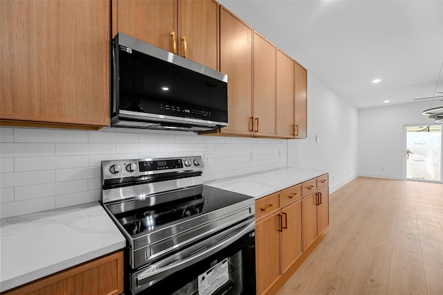 kitchen featuring tasteful backsplash, appliances with stainless steel finishes, light hardwood / wood-style floors, and light stone counters