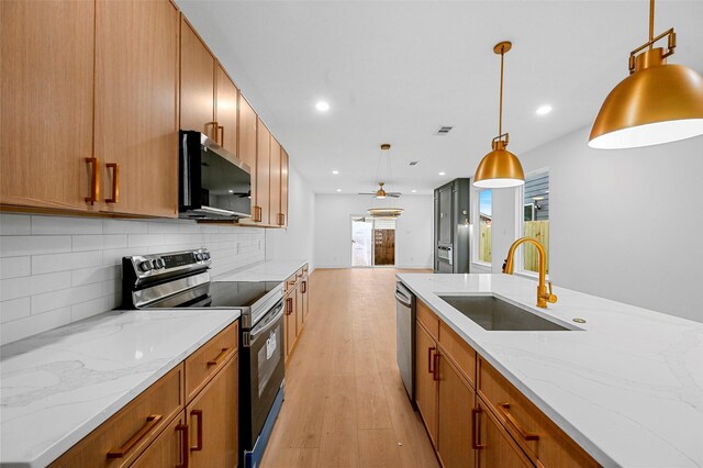 kitchen with sink, light stone counters, hanging light fixtures, stainless steel appliances, and backsplash