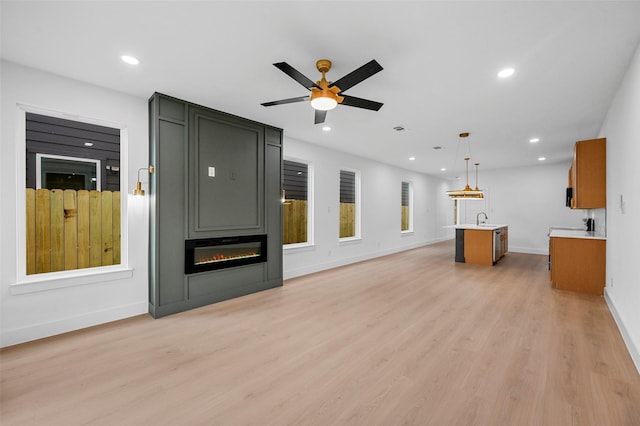 unfurnished living room featuring sink, a fireplace, light hardwood / wood-style floors, and ceiling fan