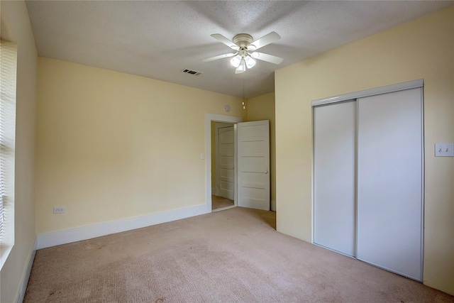 unfurnished bedroom with light carpet, a textured ceiling, ceiling fan, and a closet