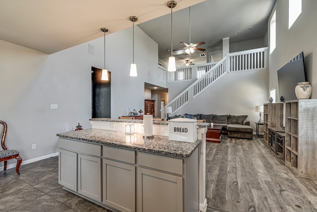 kitchen featuring decorative light fixtures, gray cabinetry, dark stone counters, a high ceiling, and ceiling fan