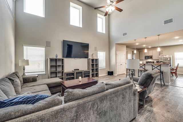 living room featuring ceiling fan, a towering ceiling, and light hardwood / wood-style floors