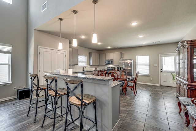 kitchen with sink, appliances with stainless steel finishes, gray cabinetry, hanging light fixtures, and a kitchen breakfast bar