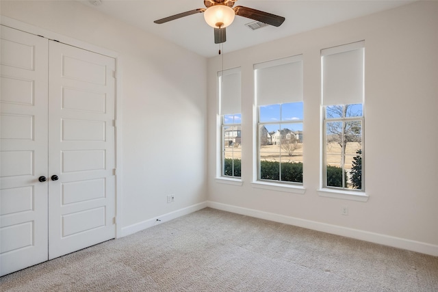 carpeted spare room with a ceiling fan, visible vents, and baseboards