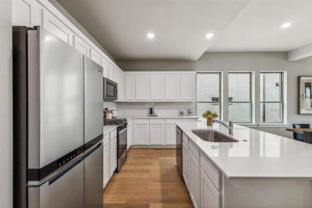 kitchen featuring sink, stainless steel appliances, white cabinets, a center island with sink, and light wood-type flooring