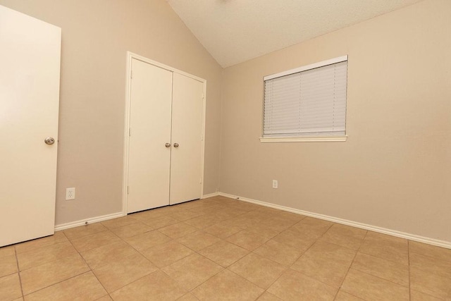 unfurnished bedroom with lofted ceiling, light tile patterned floors, and a closet