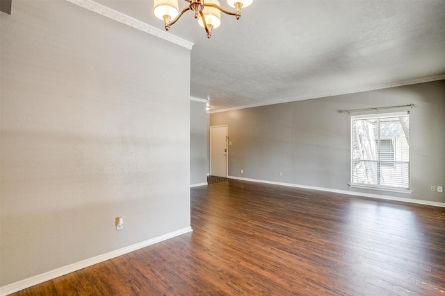 empty room with dark wood-type flooring, ornamental molding, and a chandelier