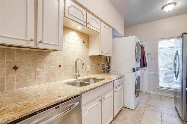 kitchen with sink, white cabinetry, stainless steel appliances, stacked washer / drying machine, and light stone countertops