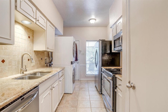 kitchen featuring stacked washer and dryer, sink, white cabinetry, light stone counters, and appliances with stainless steel finishes