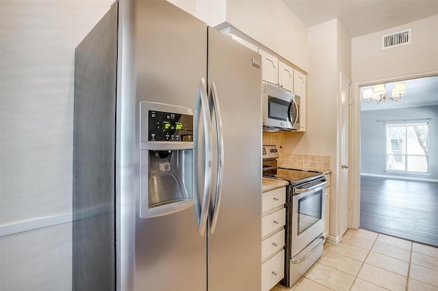 kitchen with light tile patterned floors, appliances with stainless steel finishes, backsplash, hanging light fixtures, and white cabinets