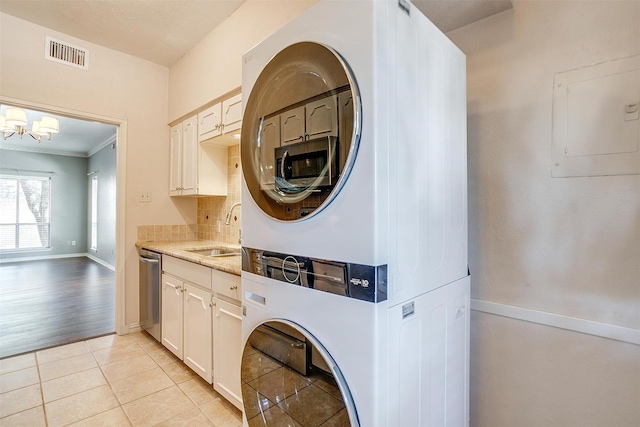 laundry room with sink, a chandelier, ornamental molding, stacked washer and clothes dryer, and light tile patterned floors