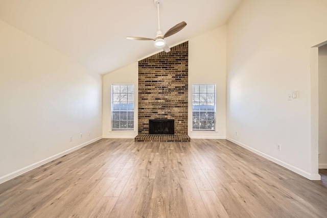 unfurnished living room featuring lofted ceiling, a brick fireplace, plenty of natural light, and light hardwood / wood-style flooring