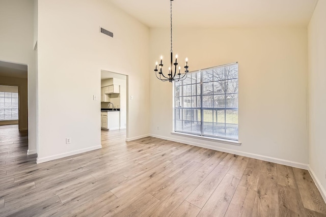 unfurnished dining area with a chandelier, high vaulted ceiling, and light wood-type flooring