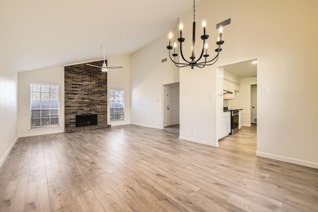 unfurnished living room with a brick fireplace, ceiling fan with notable chandelier, light hardwood / wood-style floors, and high vaulted ceiling