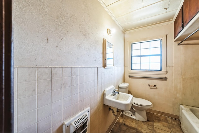 bathroom with toilet, heating unit, tile walls, ornamental molding, and a bathtub