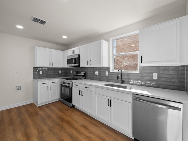 kitchen with sink, white cabinets, dark hardwood / wood-style flooring, decorative backsplash, and stainless steel appliances