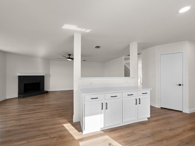 kitchen featuring white cabinetry, ceiling fan, dark wood-type flooring, and a brick fireplace