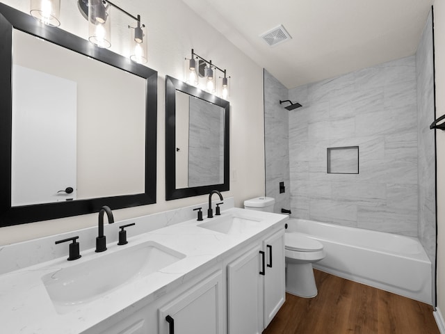 full bathroom with wood-type flooring, tiled shower / bath, vanity, and toilet