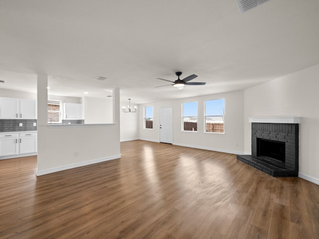 unfurnished living room with dark hardwood / wood-style floors, ceiling fan with notable chandelier, and a fireplace