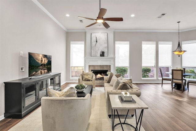 living room with crown molding, ceiling fan, wood-type flooring, and a tiled fireplace