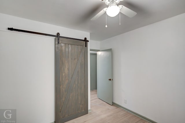 unfurnished bedroom featuring ceiling fan, a barn door, and light hardwood / wood-style flooring