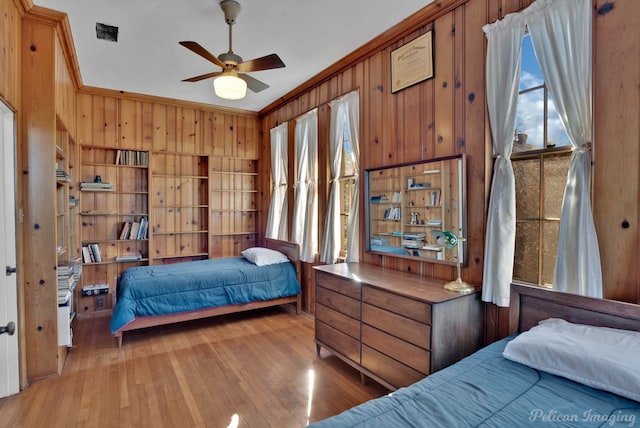 bedroom featuring crown molding, light hardwood / wood-style flooring, ceiling fan, and wood walls