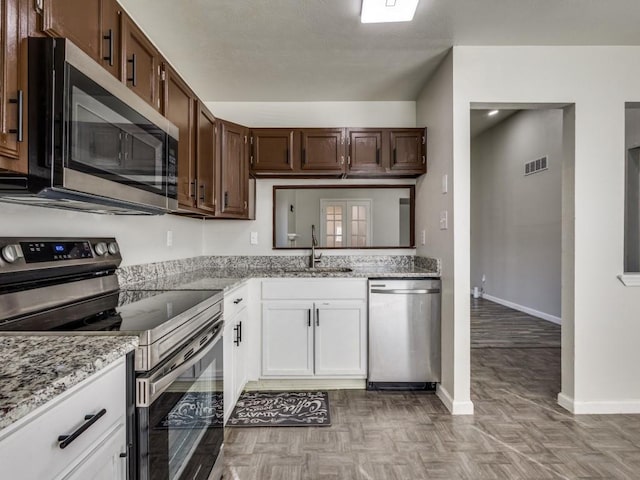 kitchen with appliances with stainless steel finishes, white cabinetry, sink, light parquet floors, and dark brown cabinetry