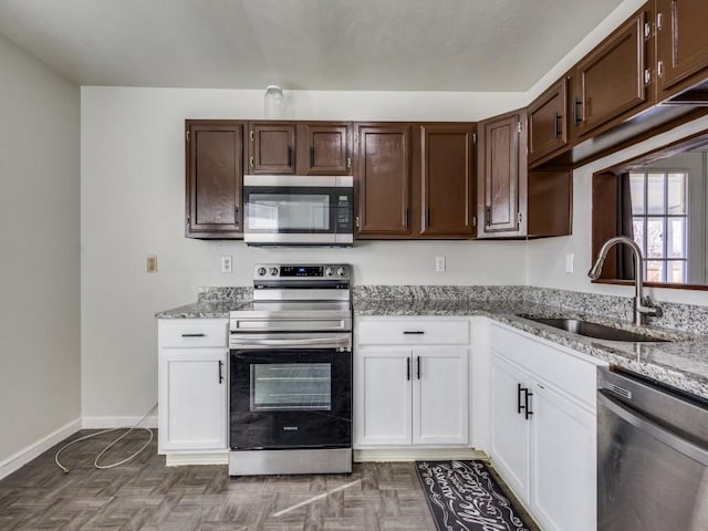 kitchen with sink, white cabinetry, stainless steel appliances, dark parquet flooring, and light stone countertops