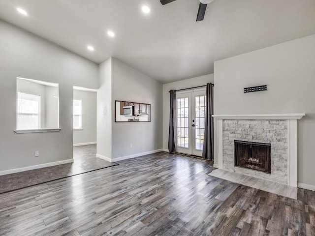 unfurnished living room featuring vaulted ceiling, a fireplace, hardwood / wood-style flooring, ceiling fan, and french doors