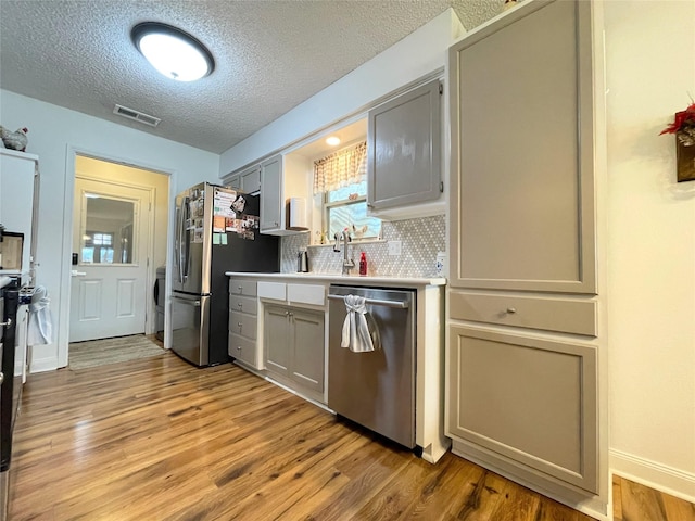 kitchen featuring appliances with stainless steel finishes, a textured ceiling, decorative backsplash, and light wood-type flooring