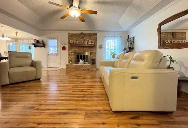 living room with ceiling fan, a tray ceiling, a brick fireplace, a textured ceiling, and light hardwood / wood-style flooring