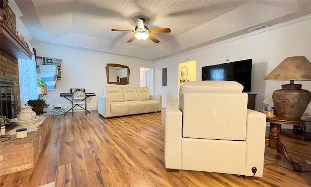 living room with hardwood / wood-style flooring, ceiling fan, a tray ceiling, a brick fireplace, and a textured ceiling