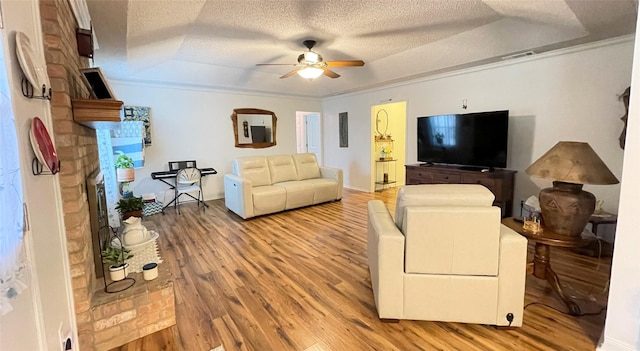 living room with ceiling fan, ornamental molding, a raised ceiling, and hardwood / wood-style floors