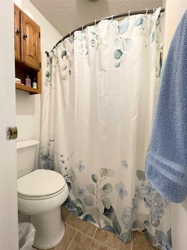 bathroom with tile patterned flooring, a shower with curtain, toilet, and a textured ceiling