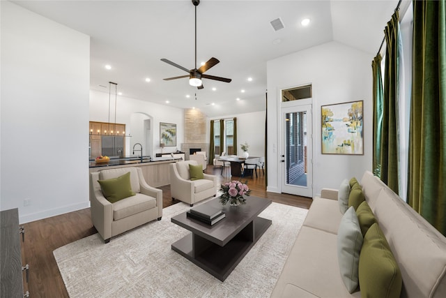 living room with sink, hardwood / wood-style flooring, ceiling fan, a large fireplace, and vaulted ceiling