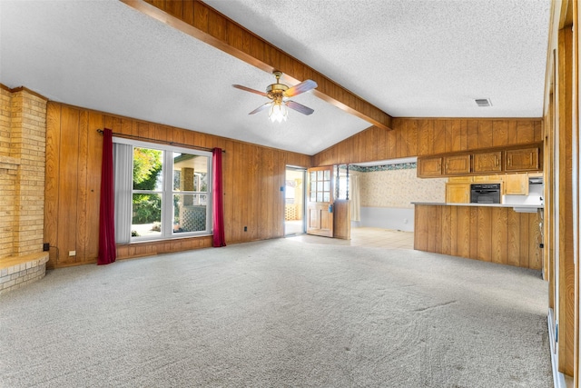 unfurnished living room with ceiling fan, vaulted ceiling with beams, wooden walls, a textured ceiling, and light carpet