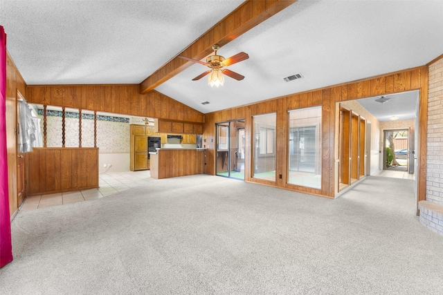 unfurnished living room featuring wooden walls, lofted ceiling with beams, light colored carpet, ceiling fan, and a textured ceiling