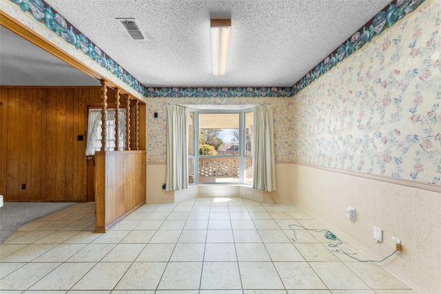 unfurnished room with tile patterned flooring, wooden walls, and a textured ceiling