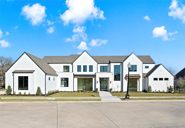 modern farmhouse featuring a shingled roof, a front lawn, and stucco siding