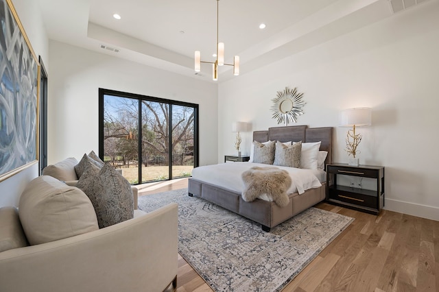 bedroom with a chandelier, visible vents, a tray ceiling, and wood finished floors