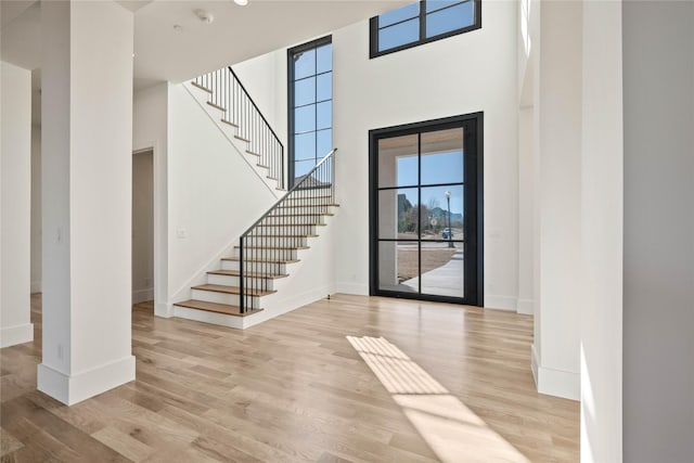 entryway featuring a towering ceiling, light wood-style floors, stairs, and baseboards