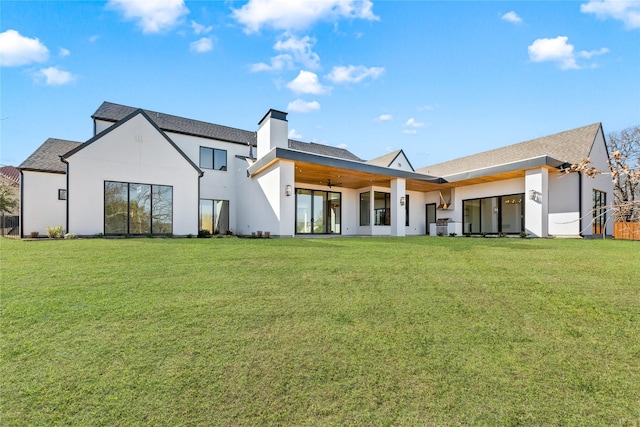 rear view of property with stucco siding, a lawn, and a chimney