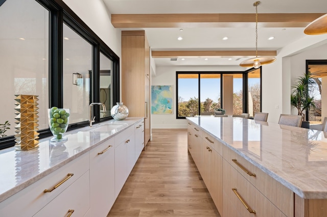 kitchen featuring light stone countertops, beam ceiling, a sink, light wood-style floors, and modern cabinets