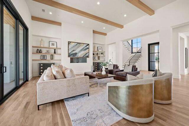 living room featuring stairway, beamed ceiling, light wood-type flooring, and baseboards