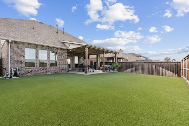 back of house featuring a fenced backyard, roof with shingles, a yard, a patio area, and brick siding