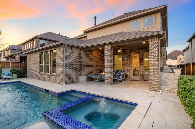 back house at dusk with exterior kitchen, a patio, pool water feature, and a pool with hot tub